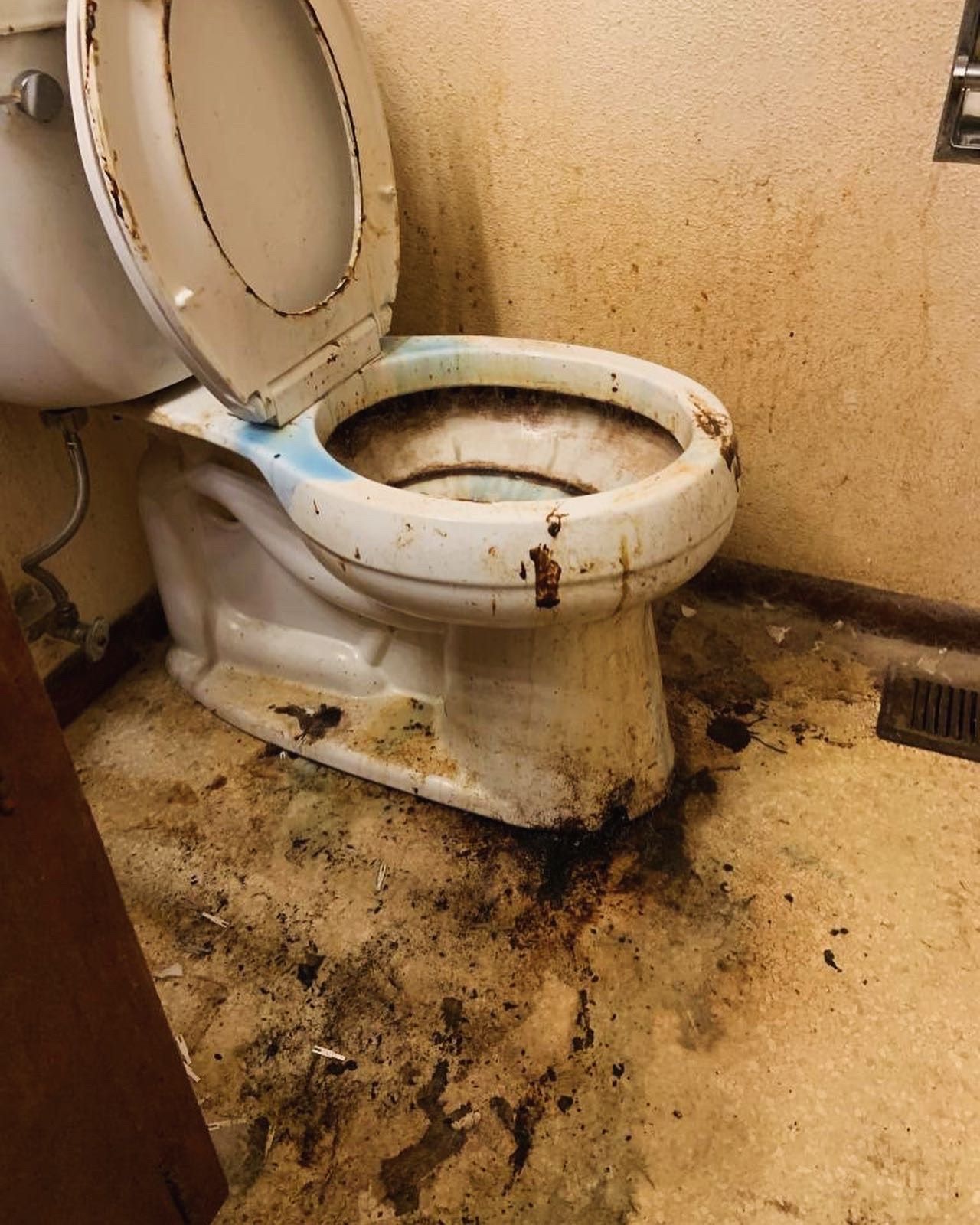 A toilet is sitting on a dirty floor in a bathroom.