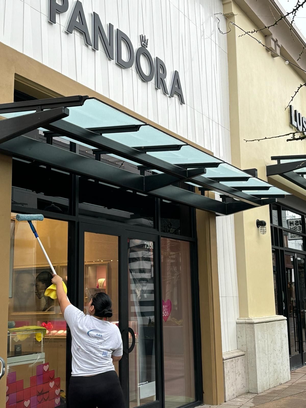 A woman is cleaning the windows of a pandora store