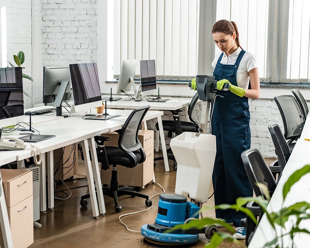 A woman is cleaning the floor of an office with a vacuum cleaner.