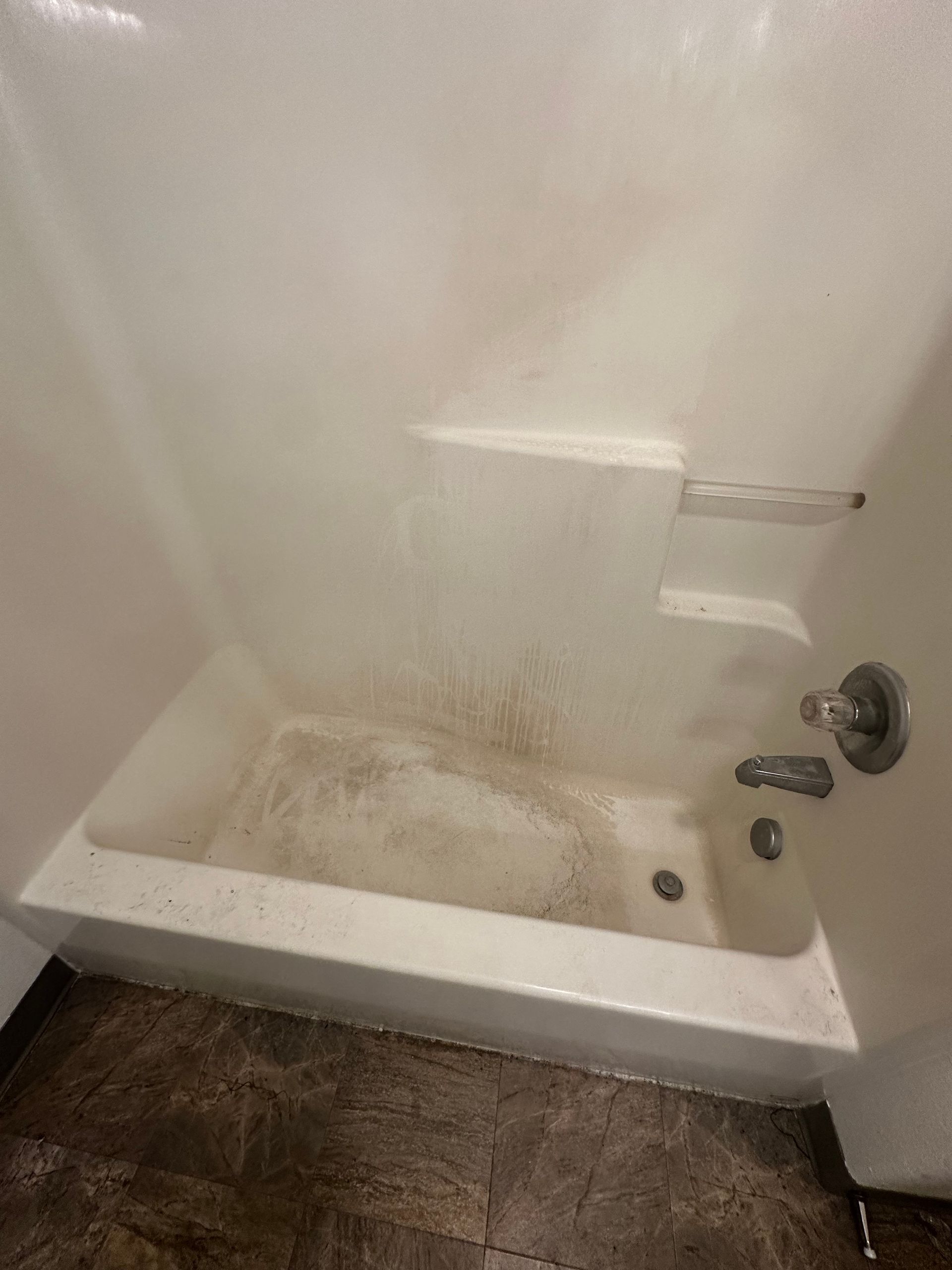 A dirty bathtub in a bathroom next to a shower.