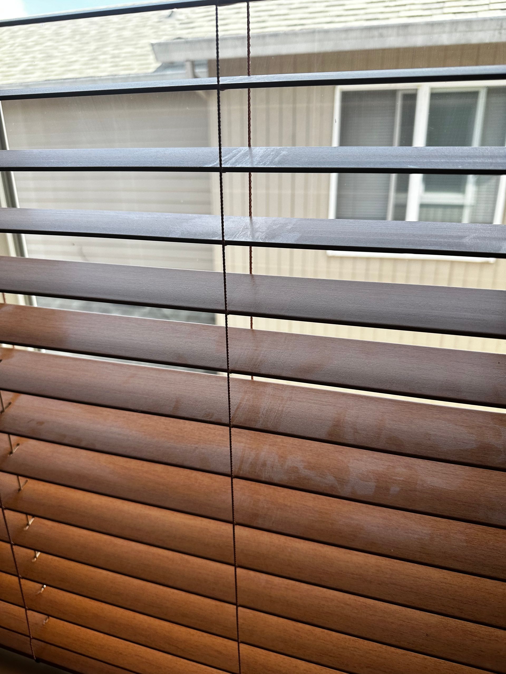 A close up of a window blind with a house in the background