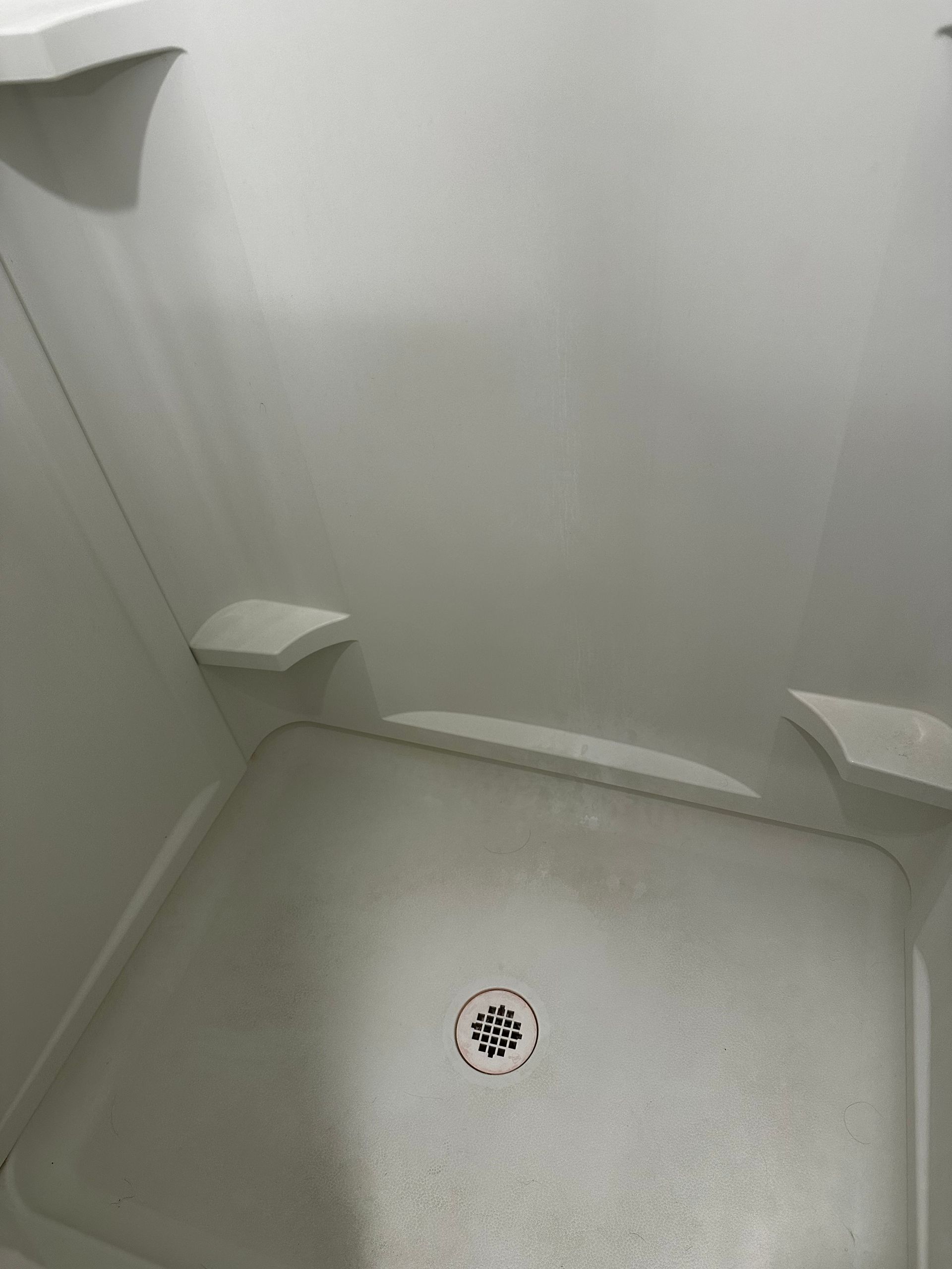 A shower stall with a drain and shelves in a bathroom.