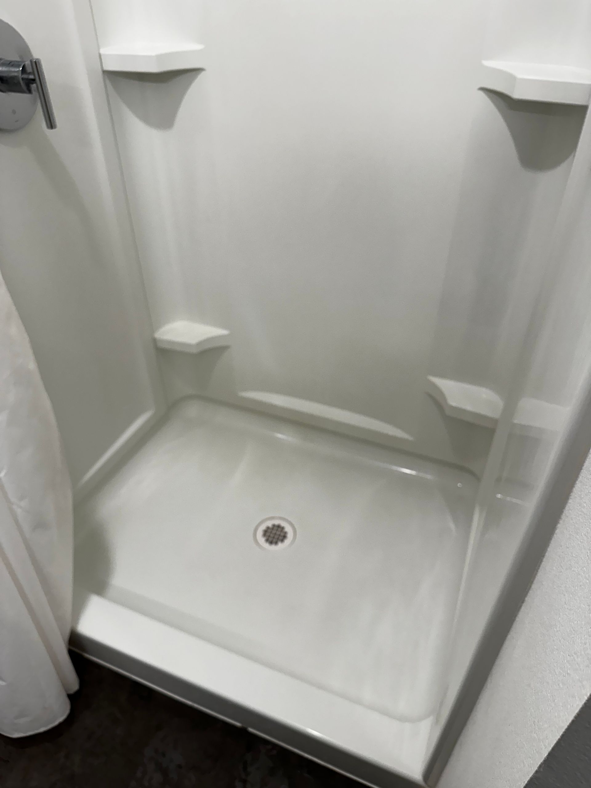 A white shower stall with shelves and a shower curtain in a bathroom.