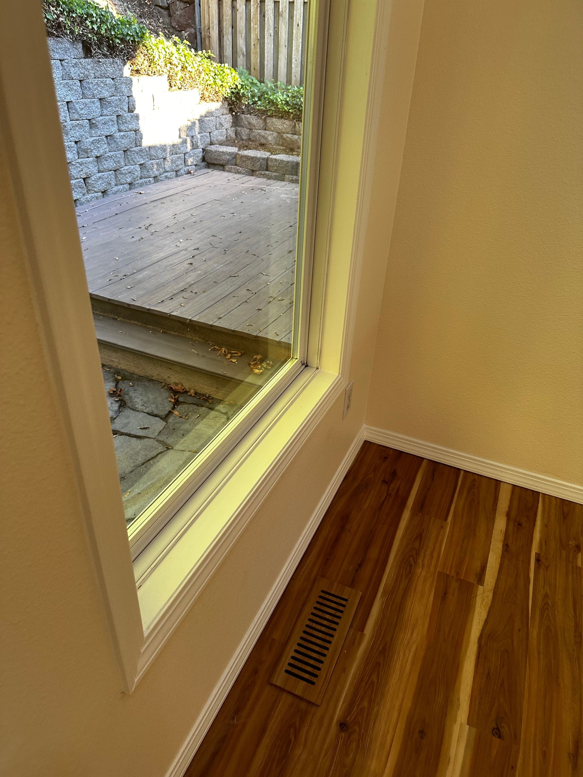 A room with hardwood floors and a window with a view of a deck.