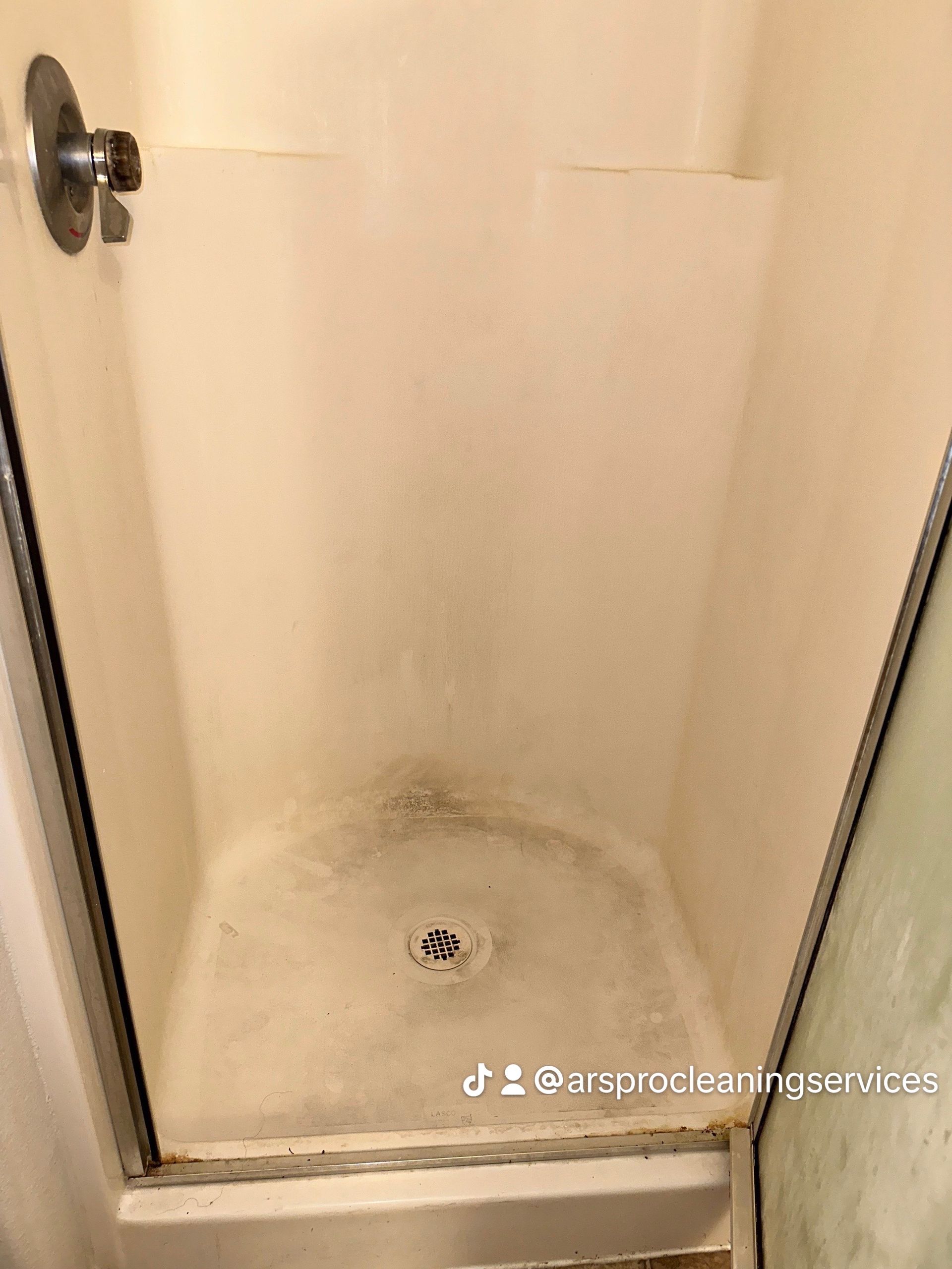 A dirty shower stall in a bathroom with a drain.