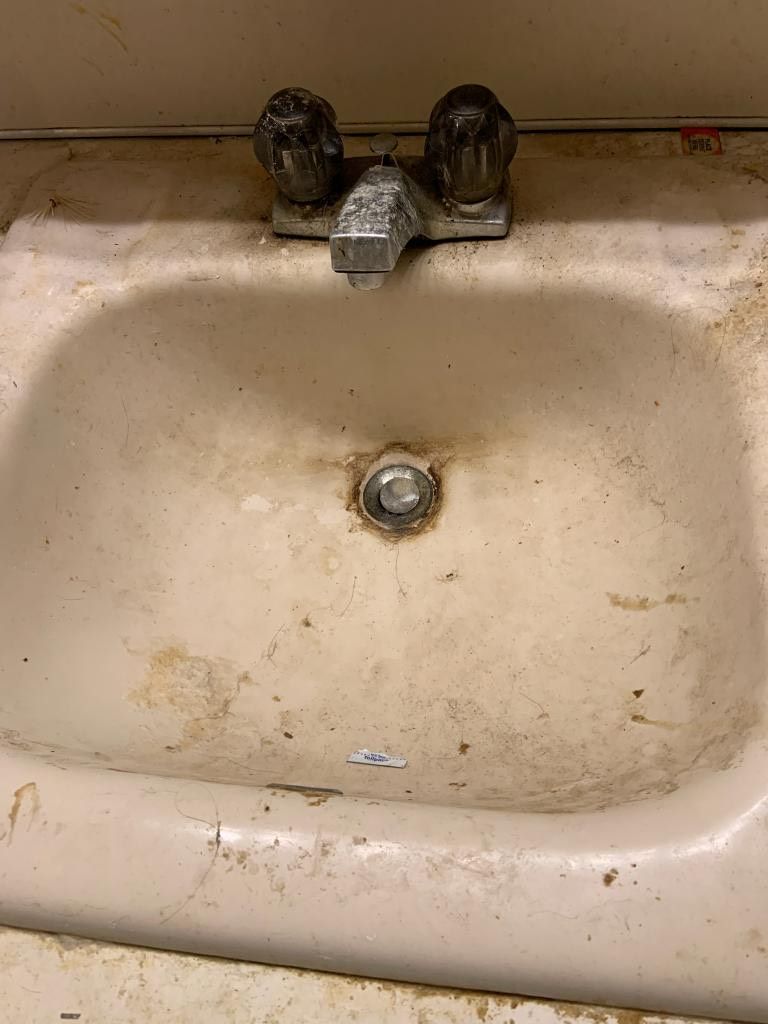 A dirty bathroom sink with a faucet and drain.