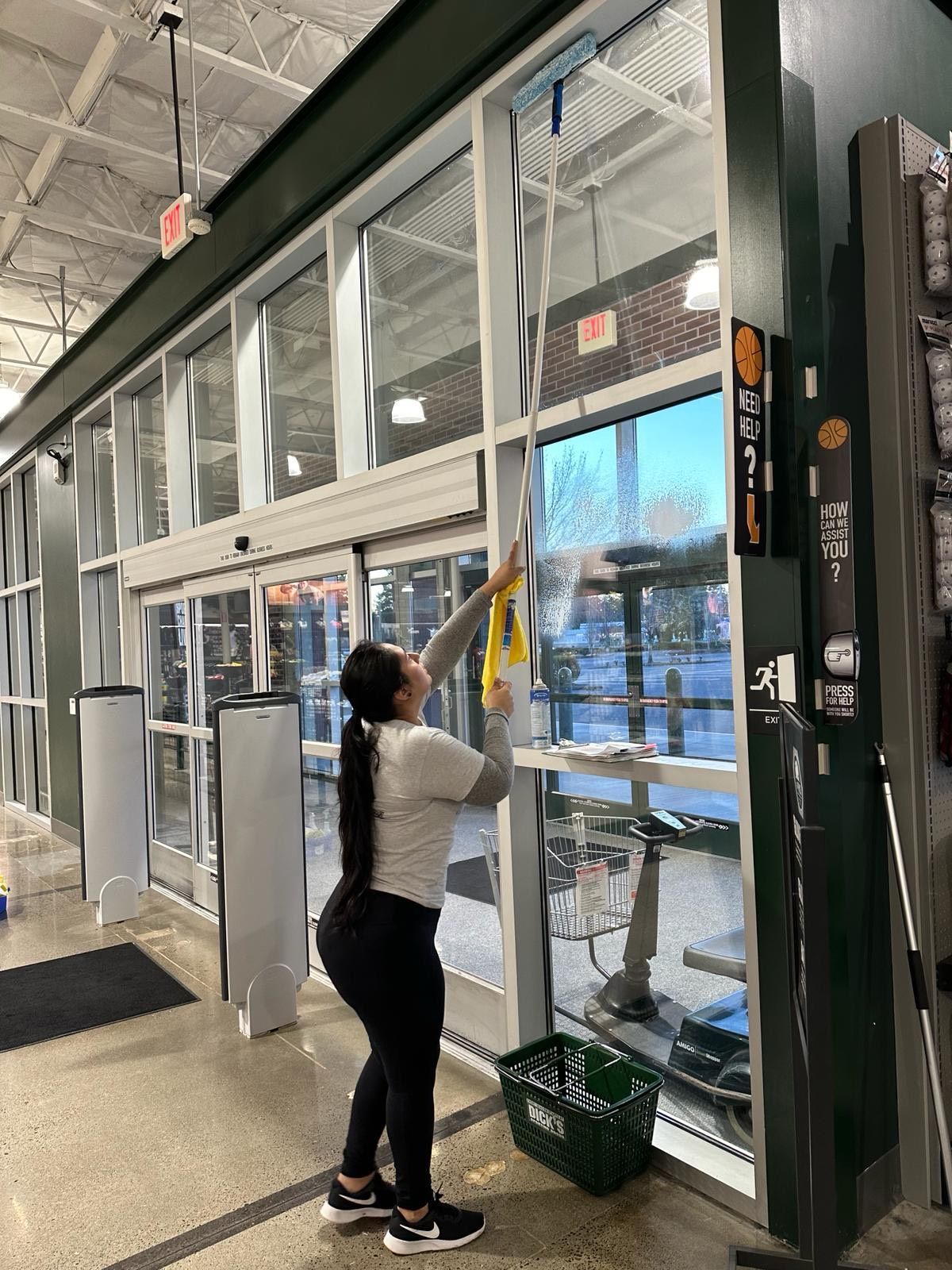 A woman is cleaning a store window with a mop.