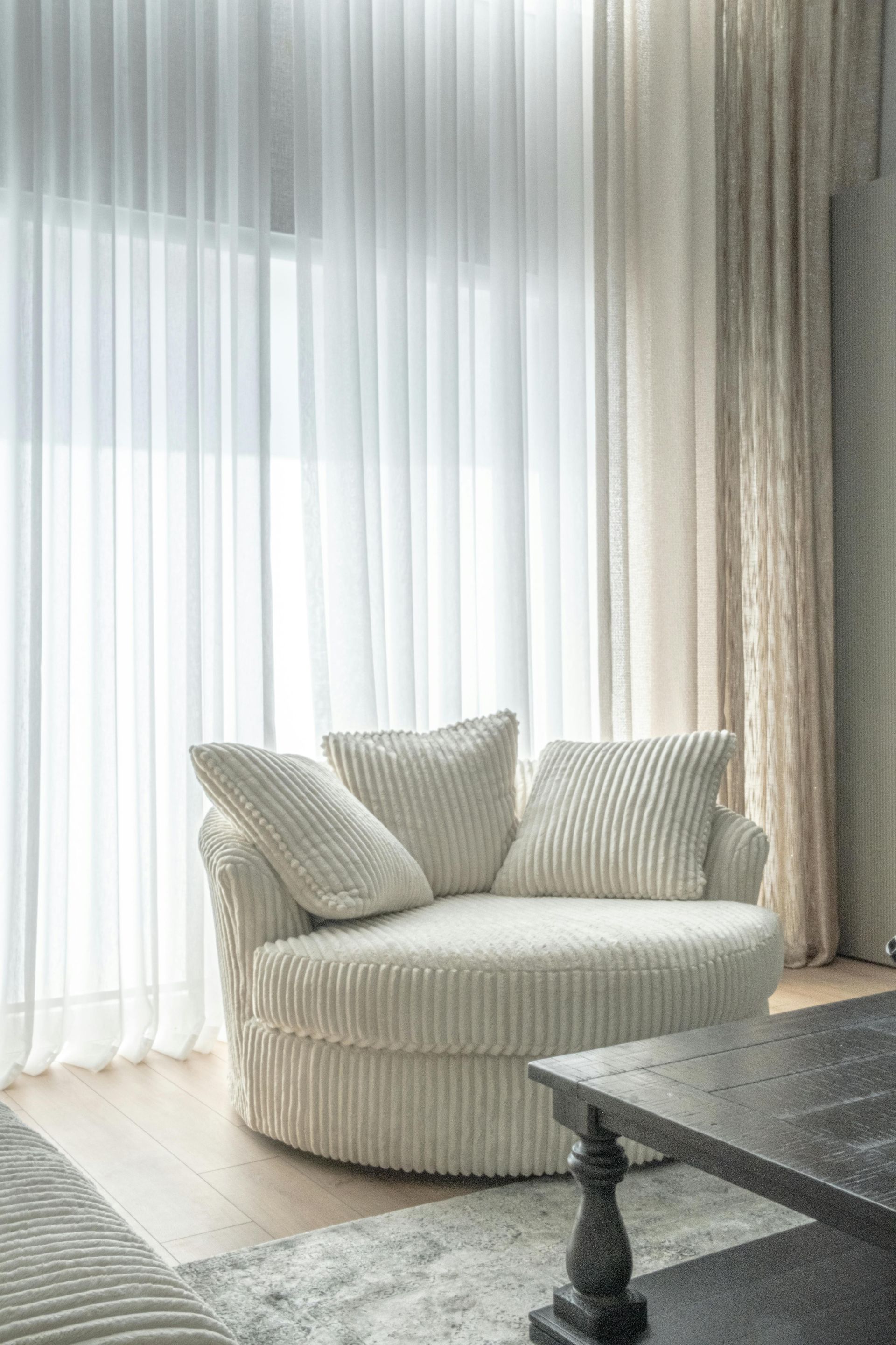 Cozy cream armchair by sheer curtains in a bright, minimalist living room