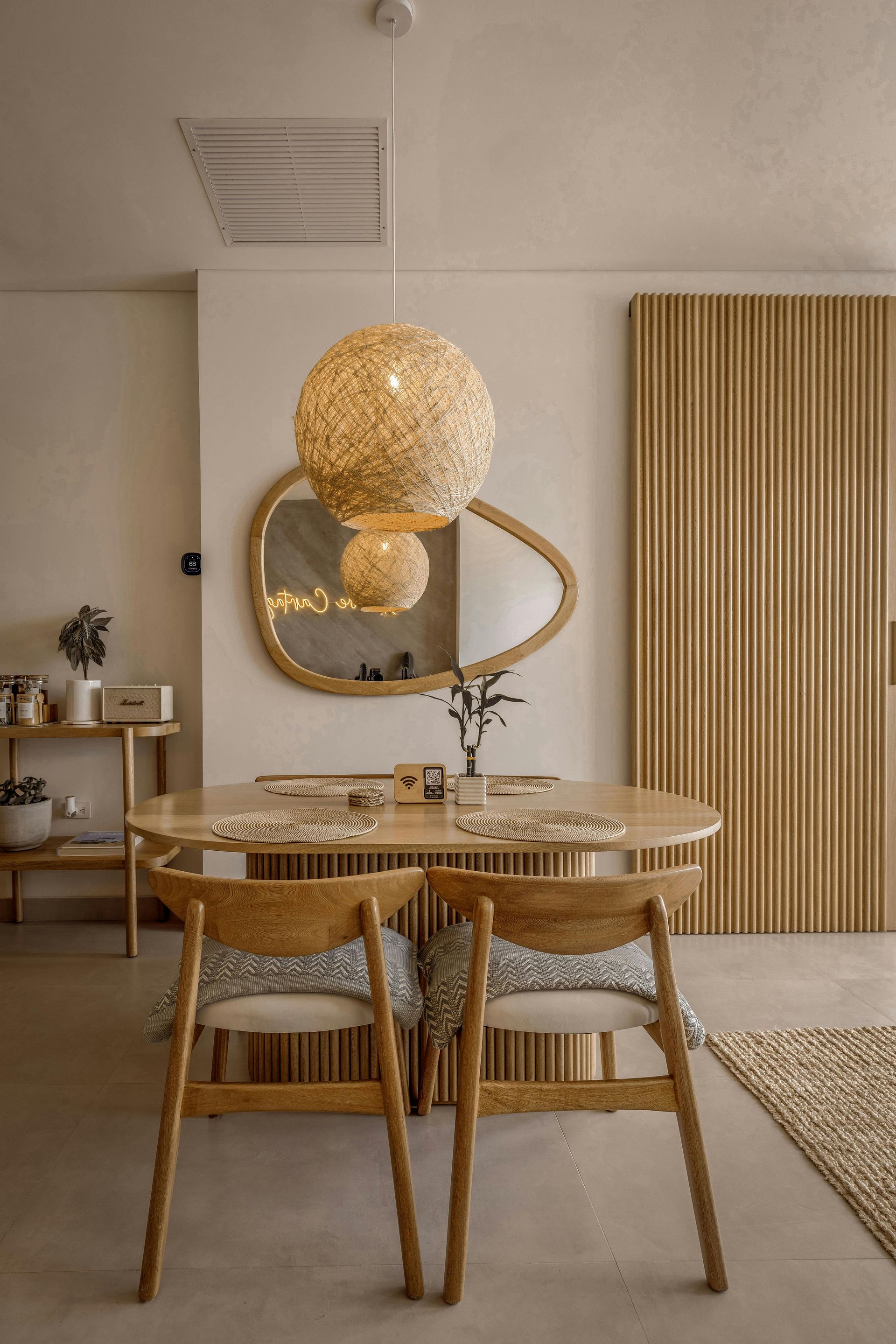 Stylish dining room with round wooden table, woven chairs, gold pendant lights, and slatted wood wall panel