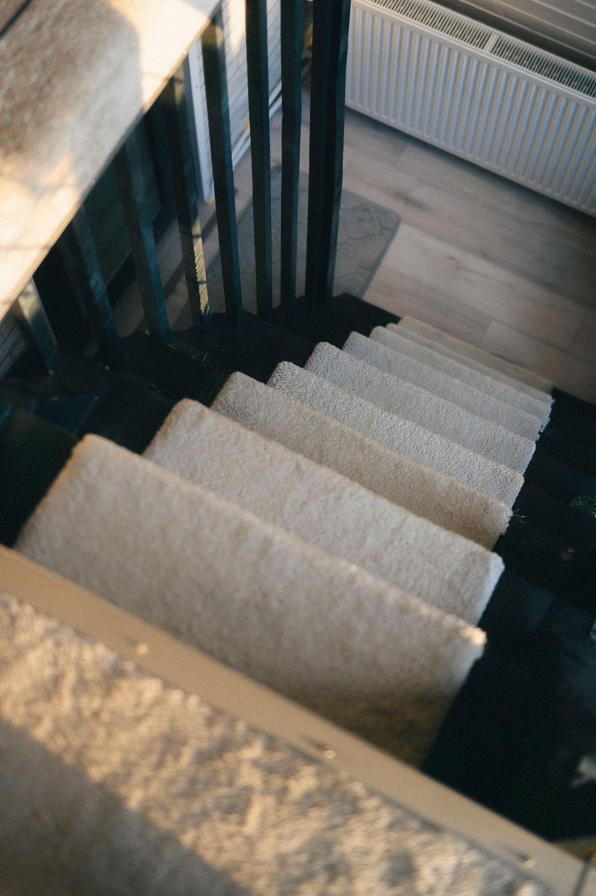 Top-down view of a carpeted staircase with black railings and a radiator beside it.
