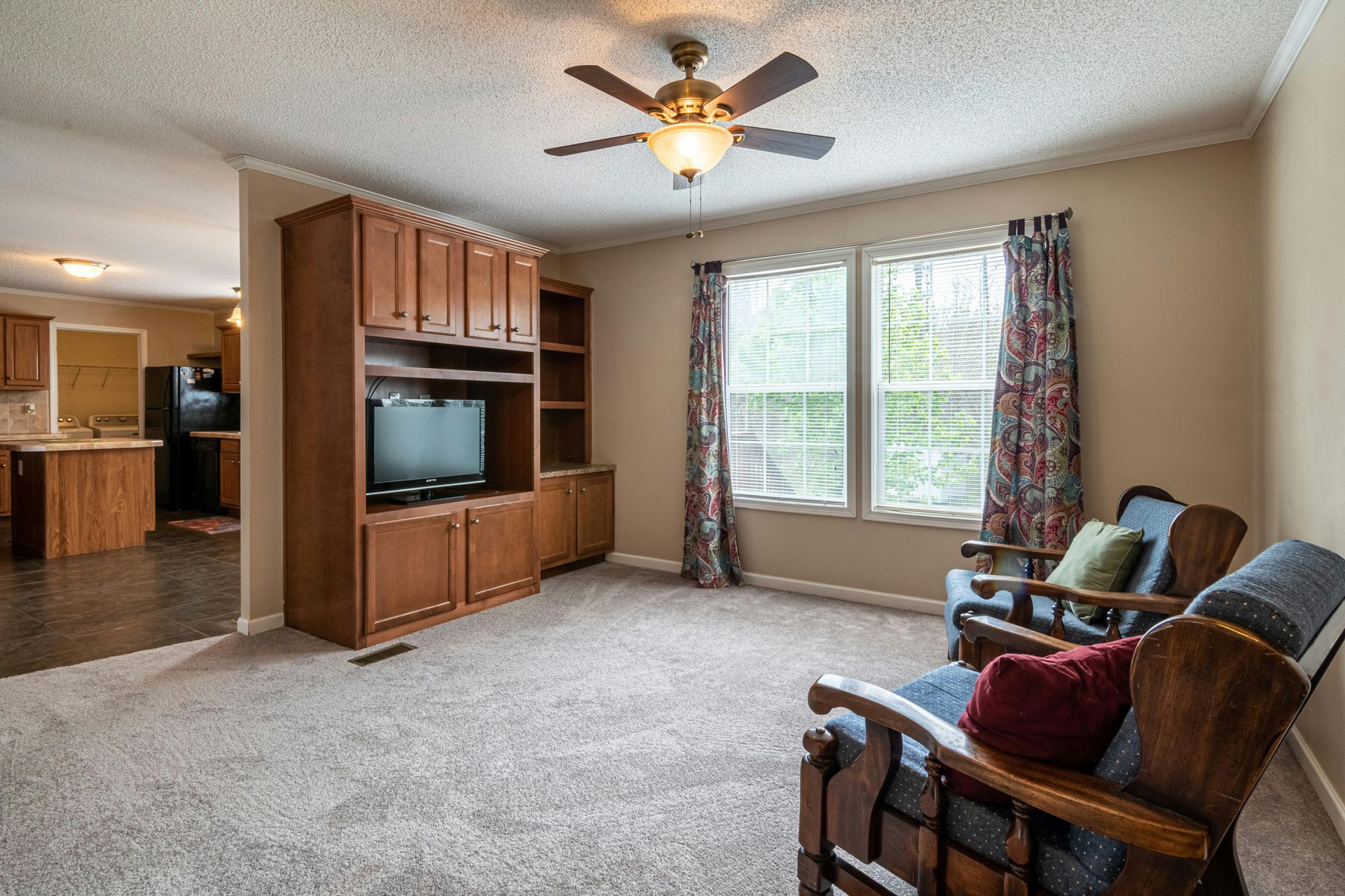 Living room with recliners, TV cabinet, ceiling fan, and a large window with floral curtains