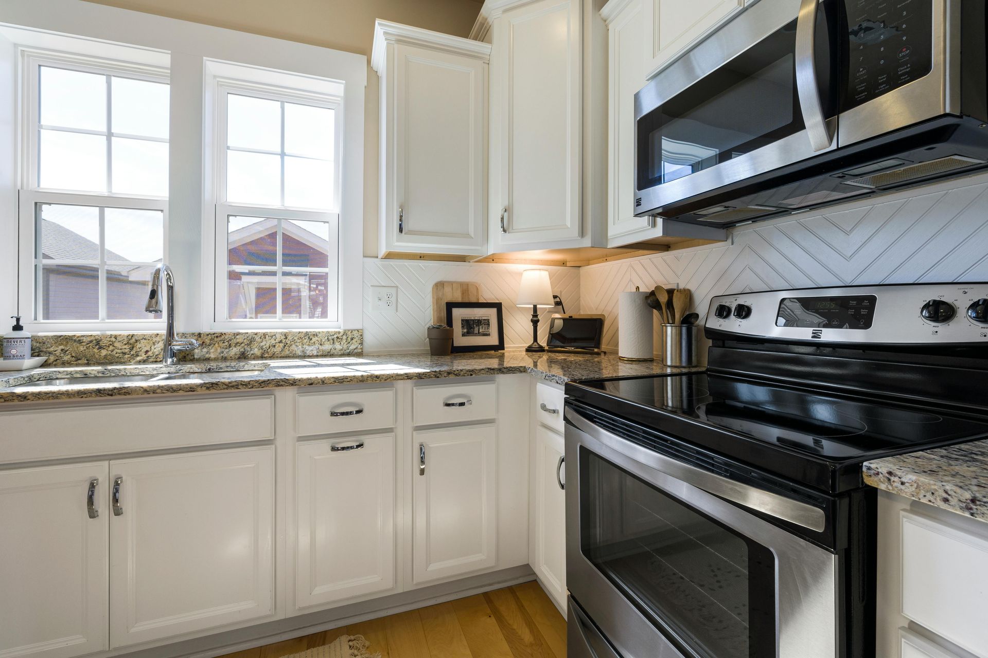 Bright white kitchen with granite countertops, stainless steel stove, microwave, and sunlight by the window