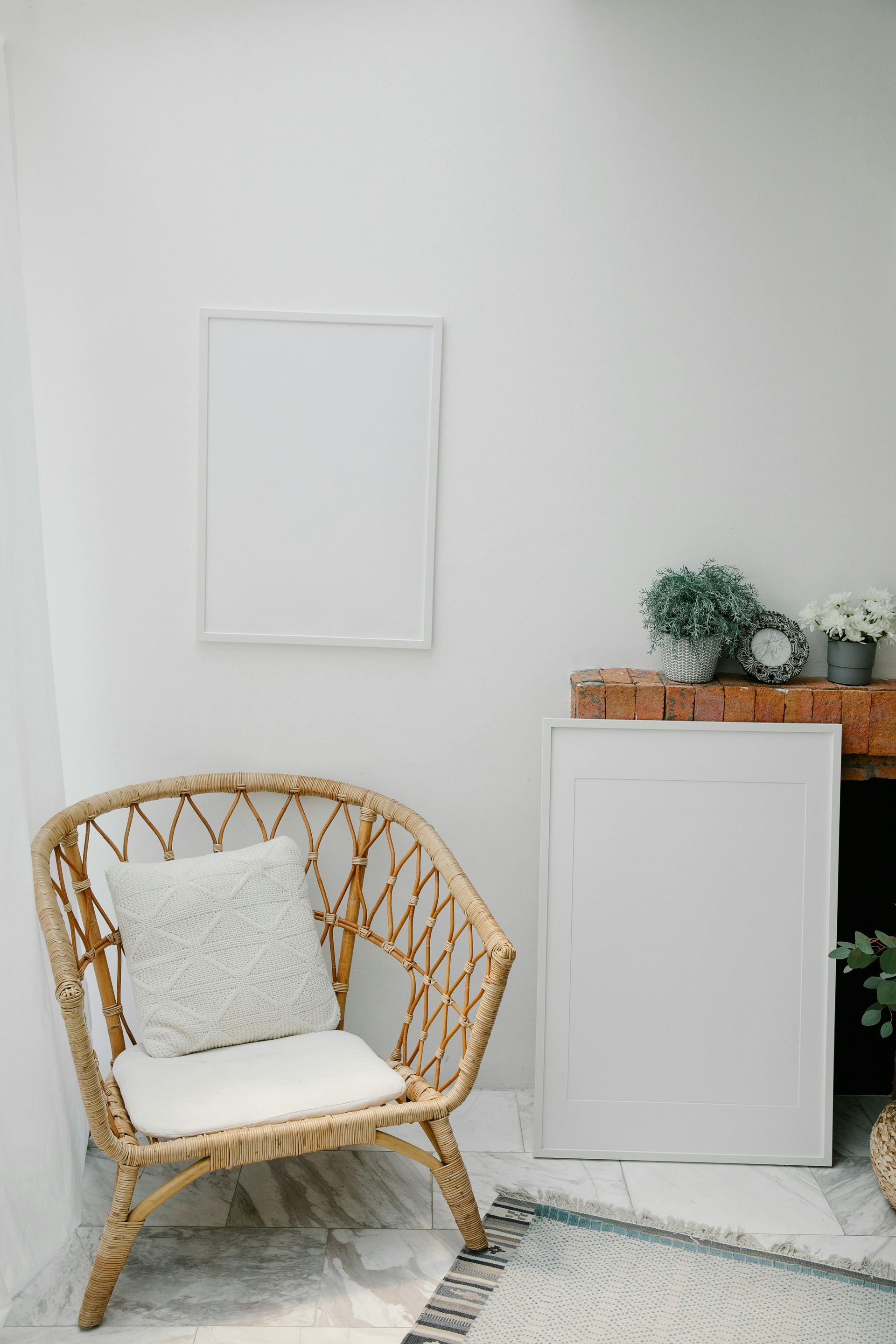 Rattan chair with white cushion beside a white cabinet and plants in a bright minimalist room