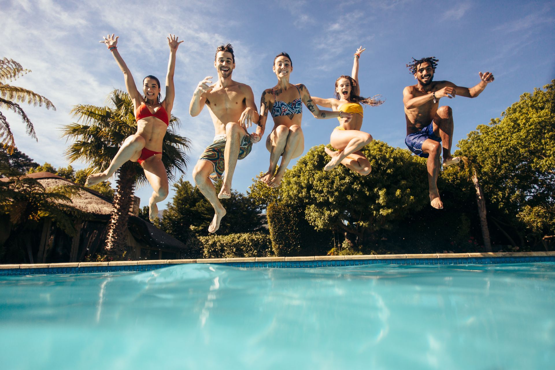 Five people jumping joyfully into a pool on a sunny day at Tradewinds Apartments