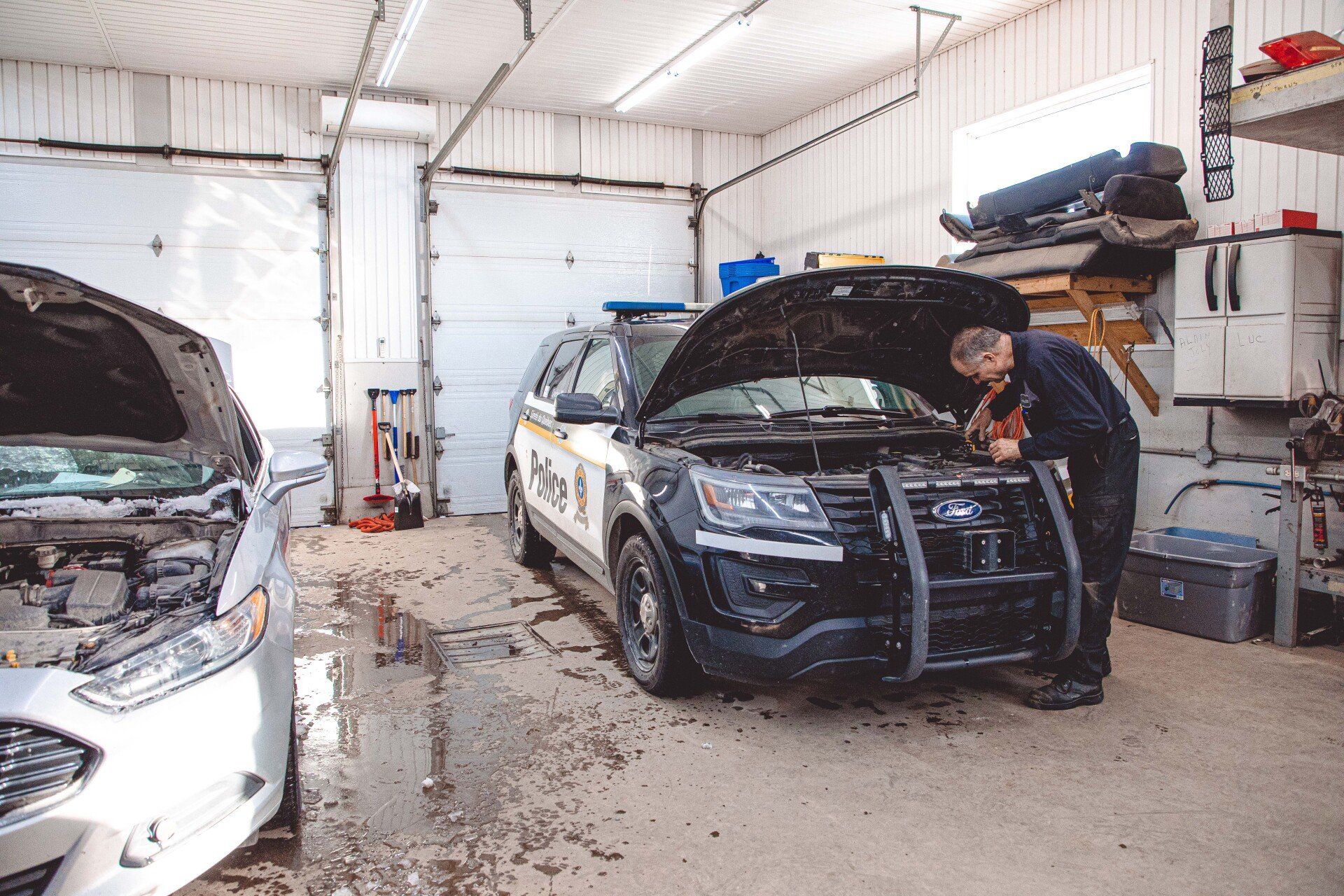 Un homme travaille sur le moteur d'une voiture de police dans un garage.