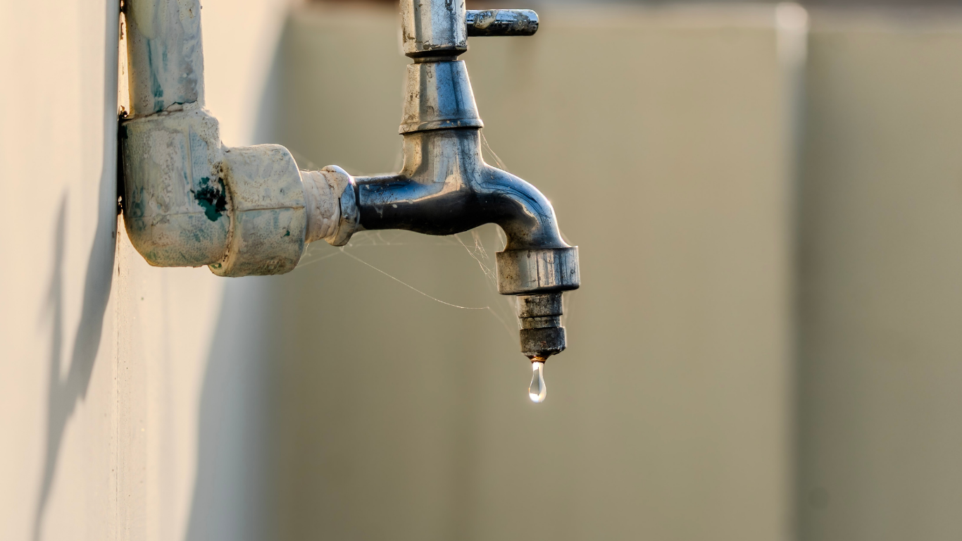 Dripping outdoor metal water tap with a small hanging droplet