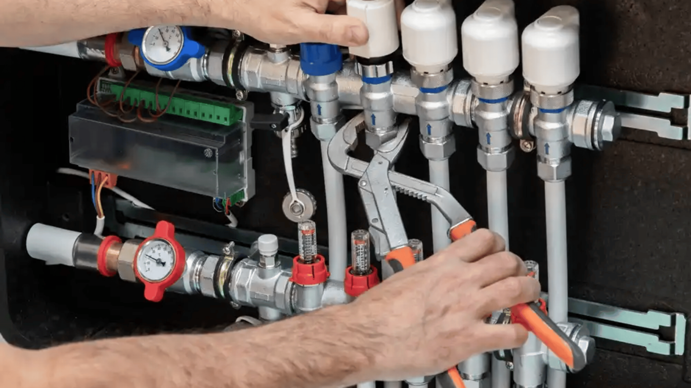 Hands adjusting pipes and valves on a white plumbing manifold with red and blue fittings.