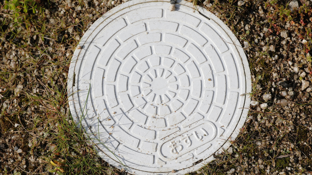 White circular manhole cover with spiral pattern set in dry grass and dirt