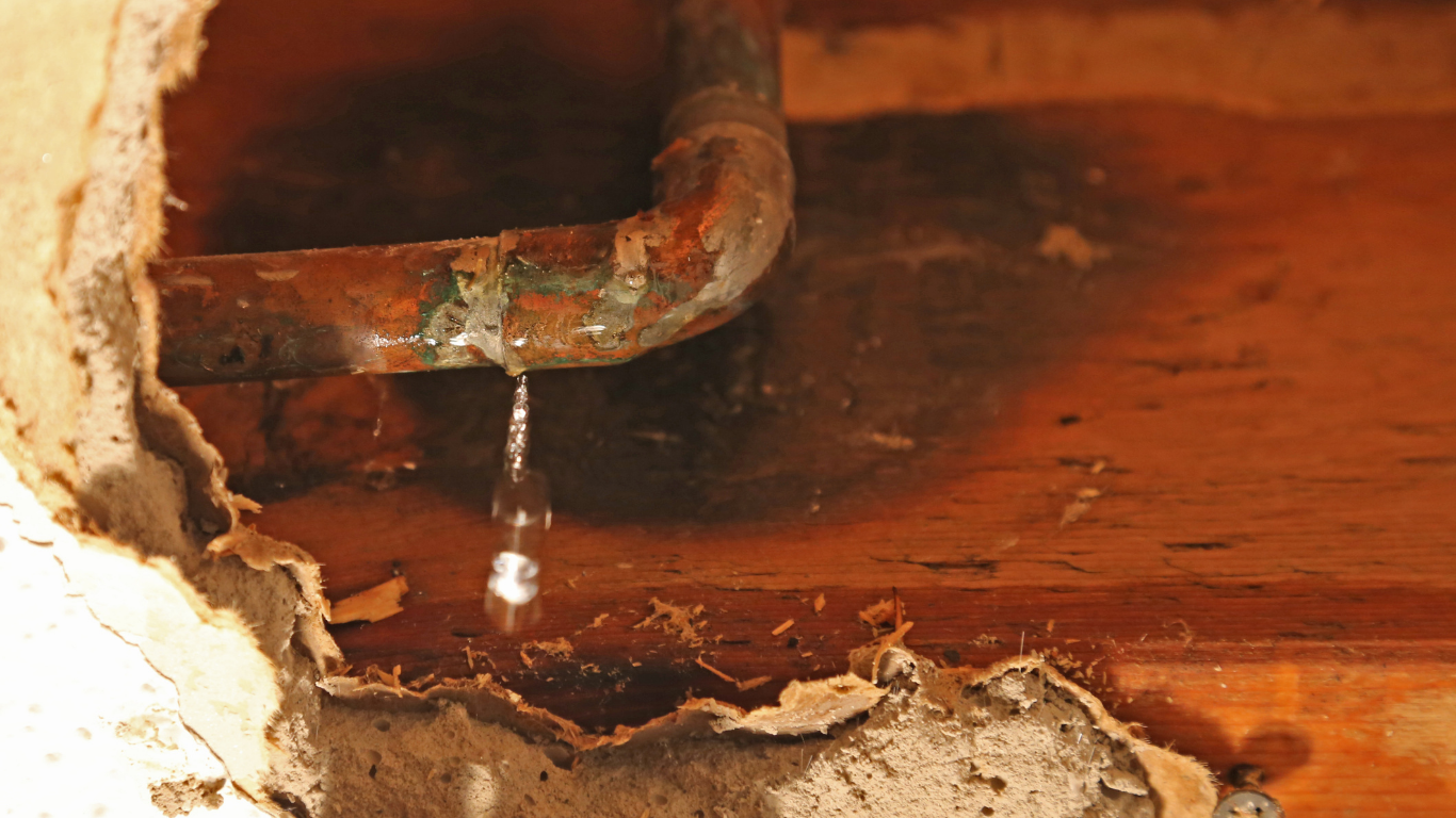 Leaking rusty pipe dripping water into a damaged wooden surface with peeling plaster