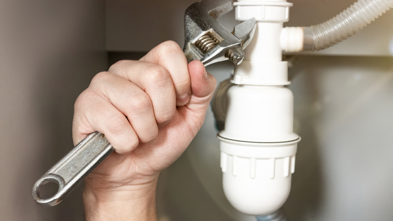 Hand tightening a wrench on a white under-sink drain pipe