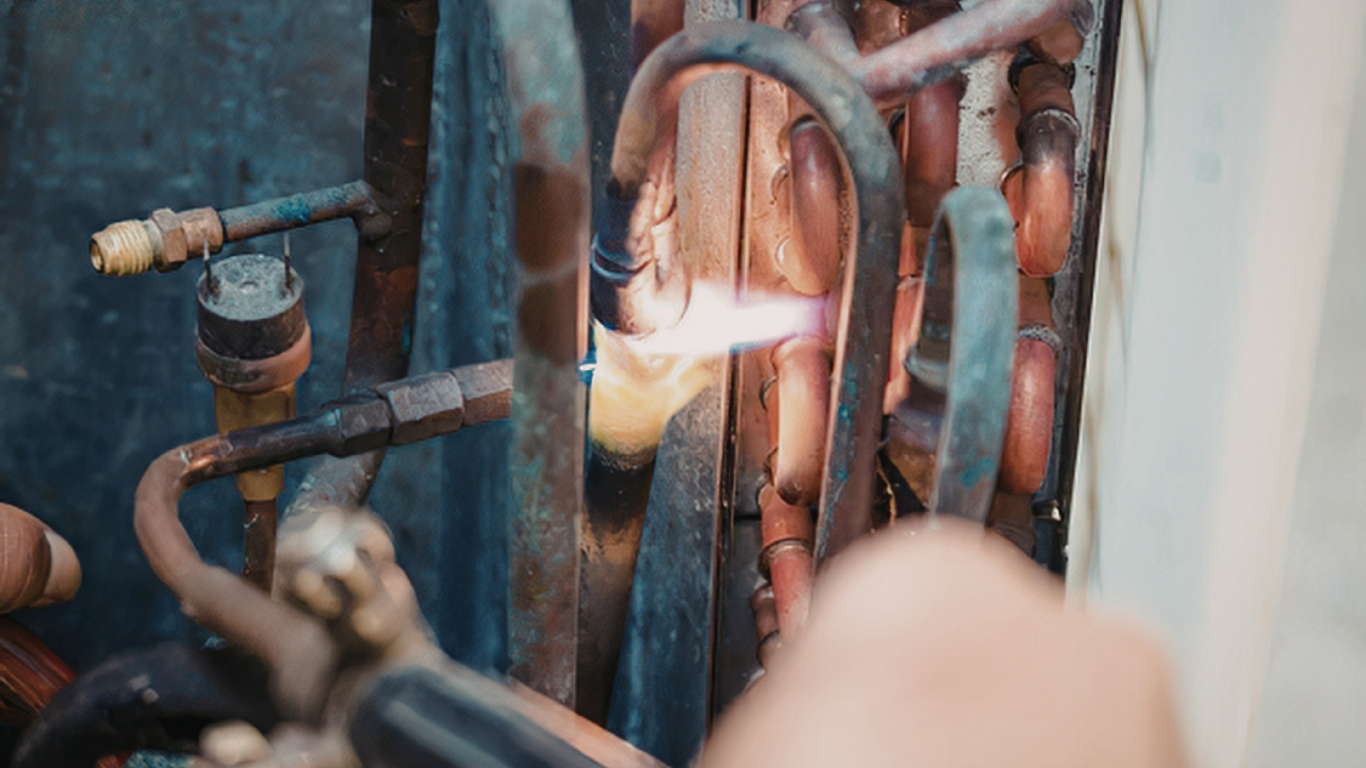 Close-up of a person soldering copper pipes with a torch in a mechanical room