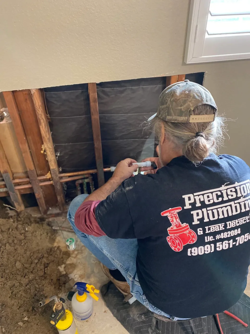 Worker kneeling in an attic beside exposed insulation and tools near a wall repair area