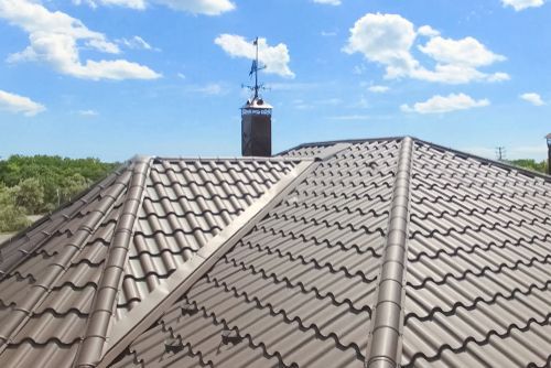 Brown metal roof with a chimney and weather station against a blue sky.