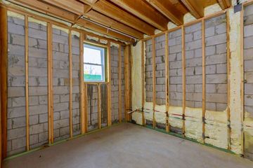Interior of a room with exposed cinder block walls, wooden frame, and insulation. Includes a window and wooden ceiling.