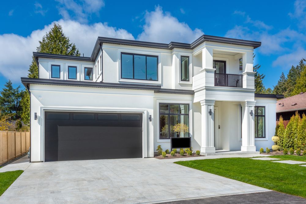 Two-story modern white house with black trim, a garage, and a concrete driveway on a sunny day.