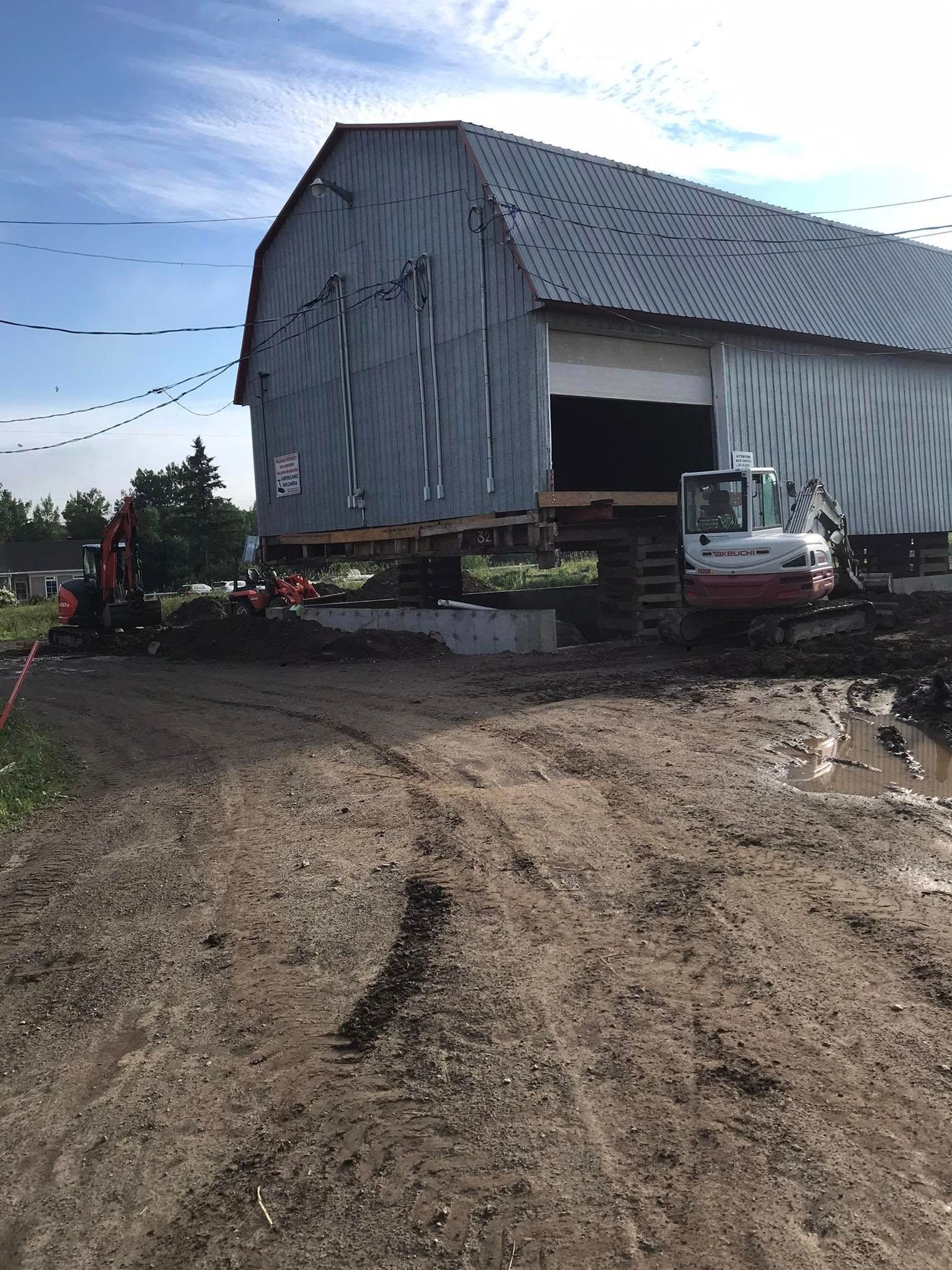 Grange soulevée par des machines pendant la construction par une journée boueuse et nuageuse.