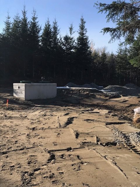 Chantier de construction avec fosse septique, tas de gravier et arrière-plan forestier.