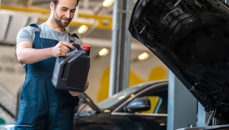 A man is pouring oil into a car in a garage. | Import Specialty Service