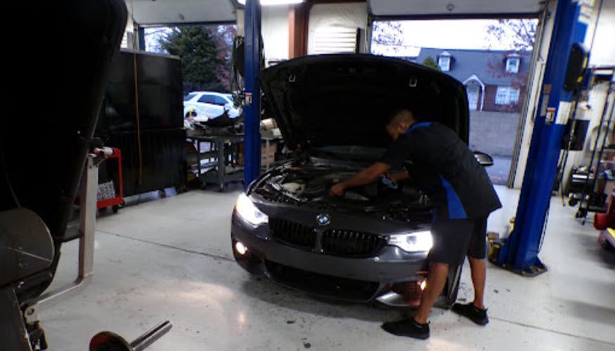 A man is working on the engine of a car in a garage. | Import Specialty Service