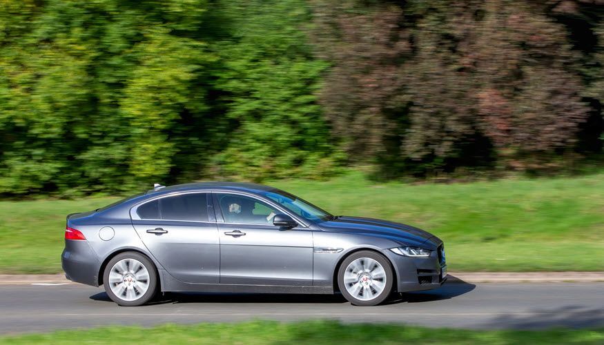 A gray car is driving down a road next to a grassy field. | Import Specialty Service