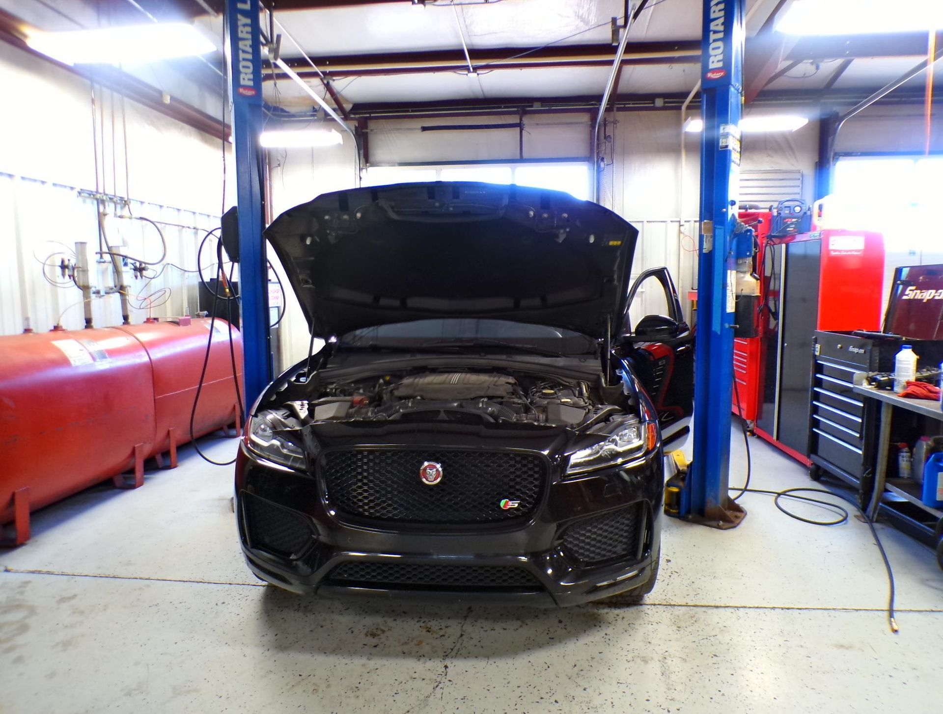 A black car with the hood up is on a lift in a garage. | Import Specialty Service