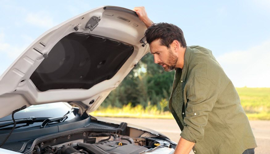 A man is looking under the hood of a broken down car. | Import Specialty Service
