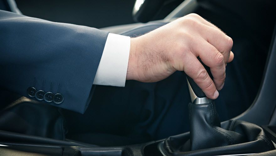 A man in a suit is changing gears in a car. | Import Specialty Service