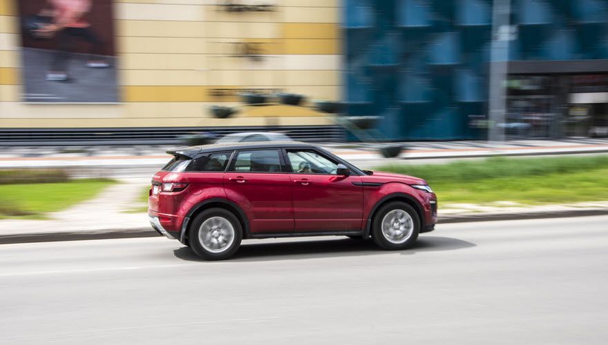 A red car is driving down a city street. | Import Specialty Service
