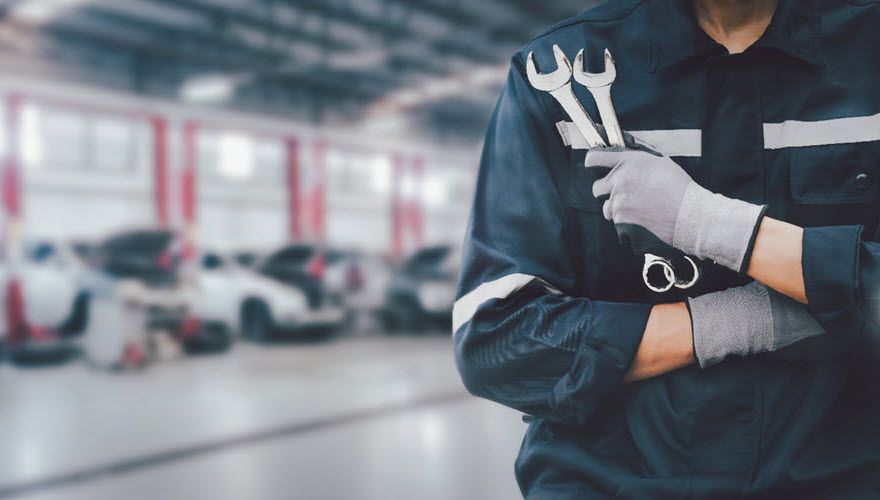 A mechanic is holding two wrenches in a garage. | Import Specialty Service