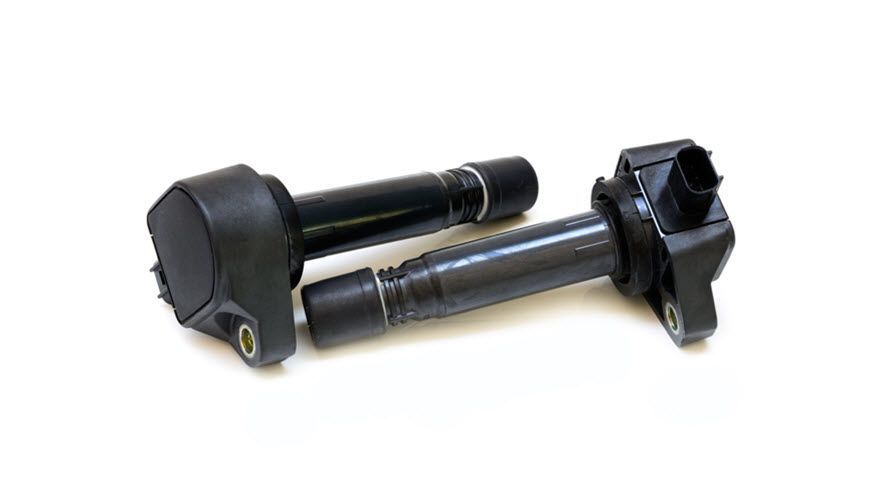 Two ignition coils are sitting next to each other on a white surface. | Import Specialty Service