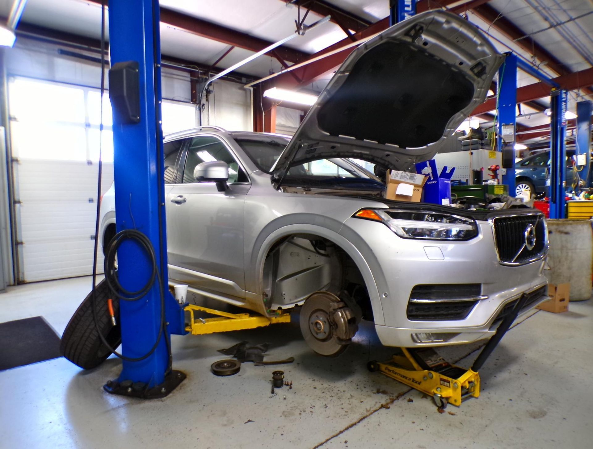 A silver car with the hood up is on a lift in a garage. | Import Specialty Service