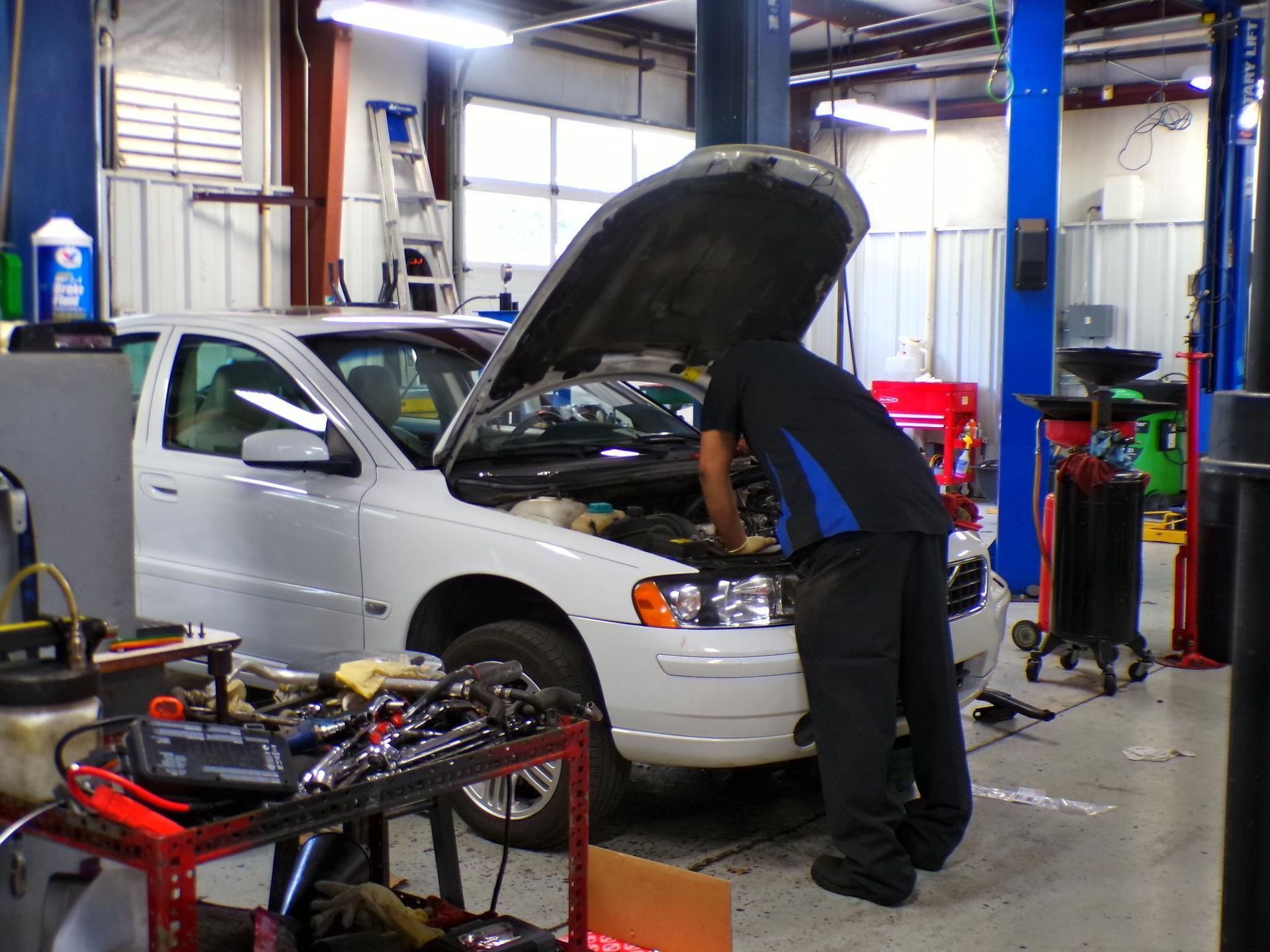 A man is working on a car in a garage with the hood up | Import Specialty Service