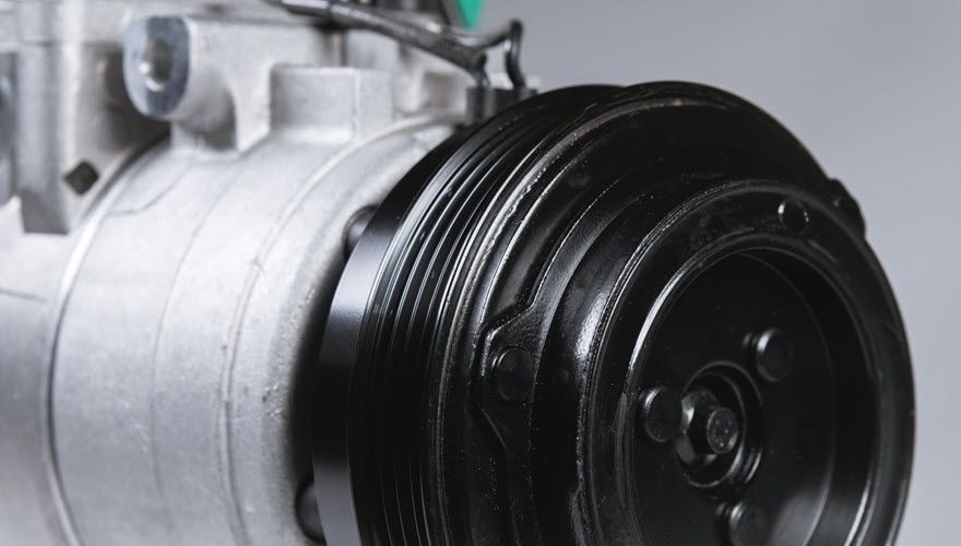 A close up of a car air conditioner compressor on a gray background. | Import Specialty Service