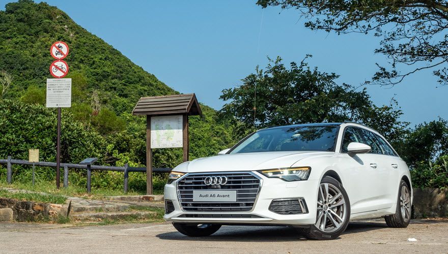 A white audi a6 is parked in a parking lot in front of a mountain. | Import Specialty Service