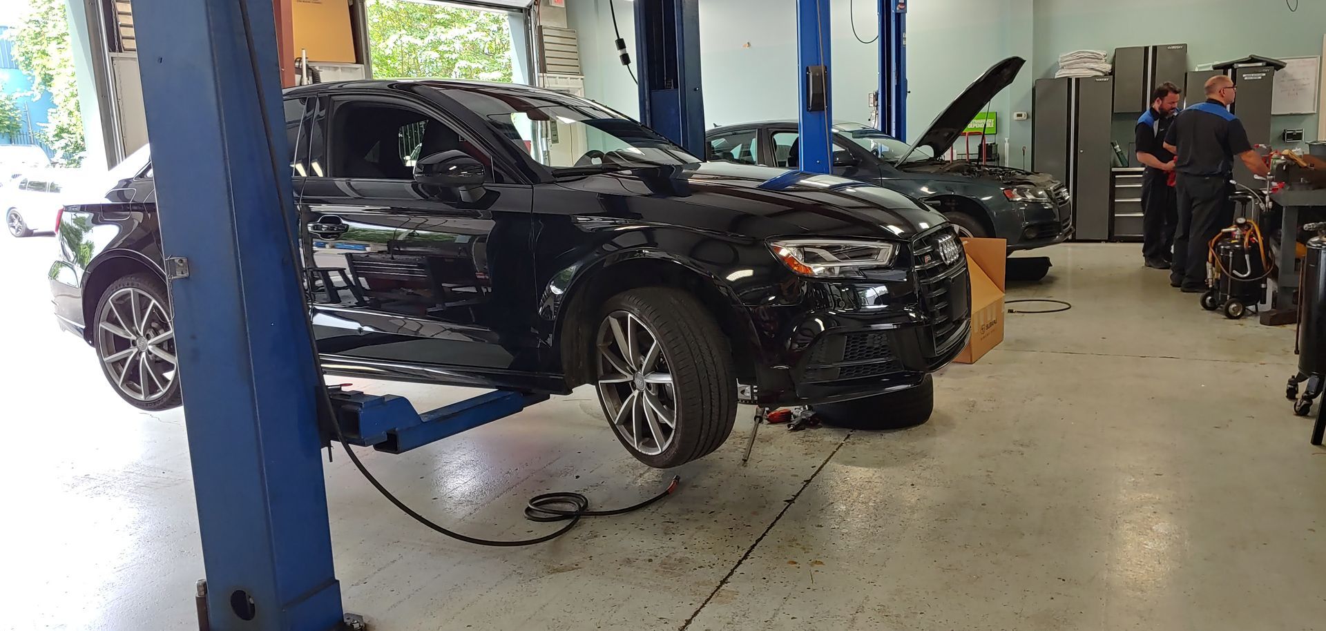 A black car is on a lift in a garage. | Import Specialty Service