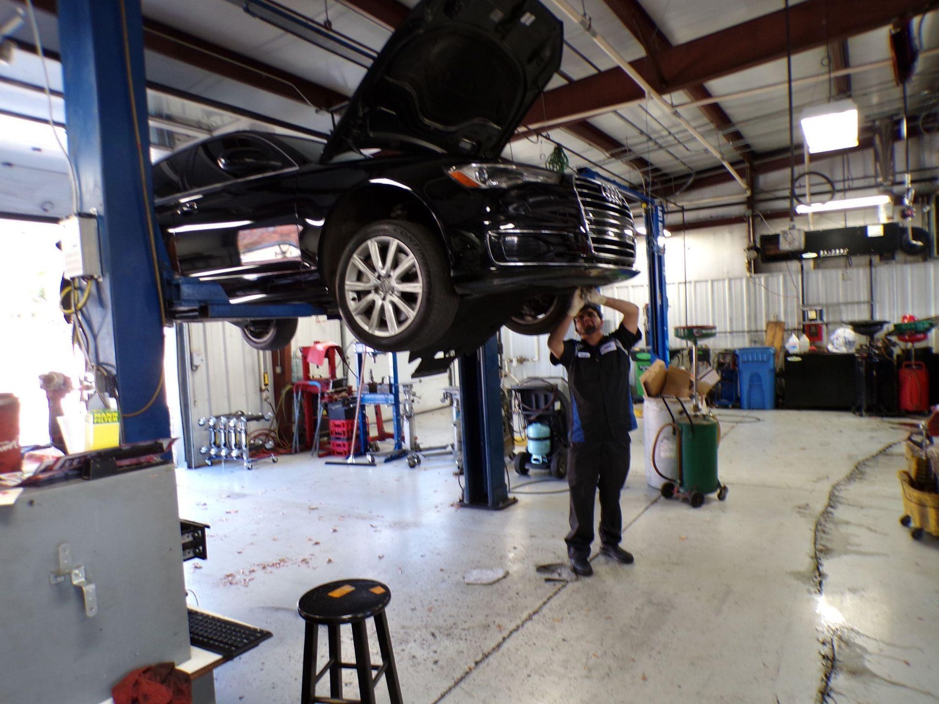 A man is working on a car in a garage with the hood up. | Import Specialty Service