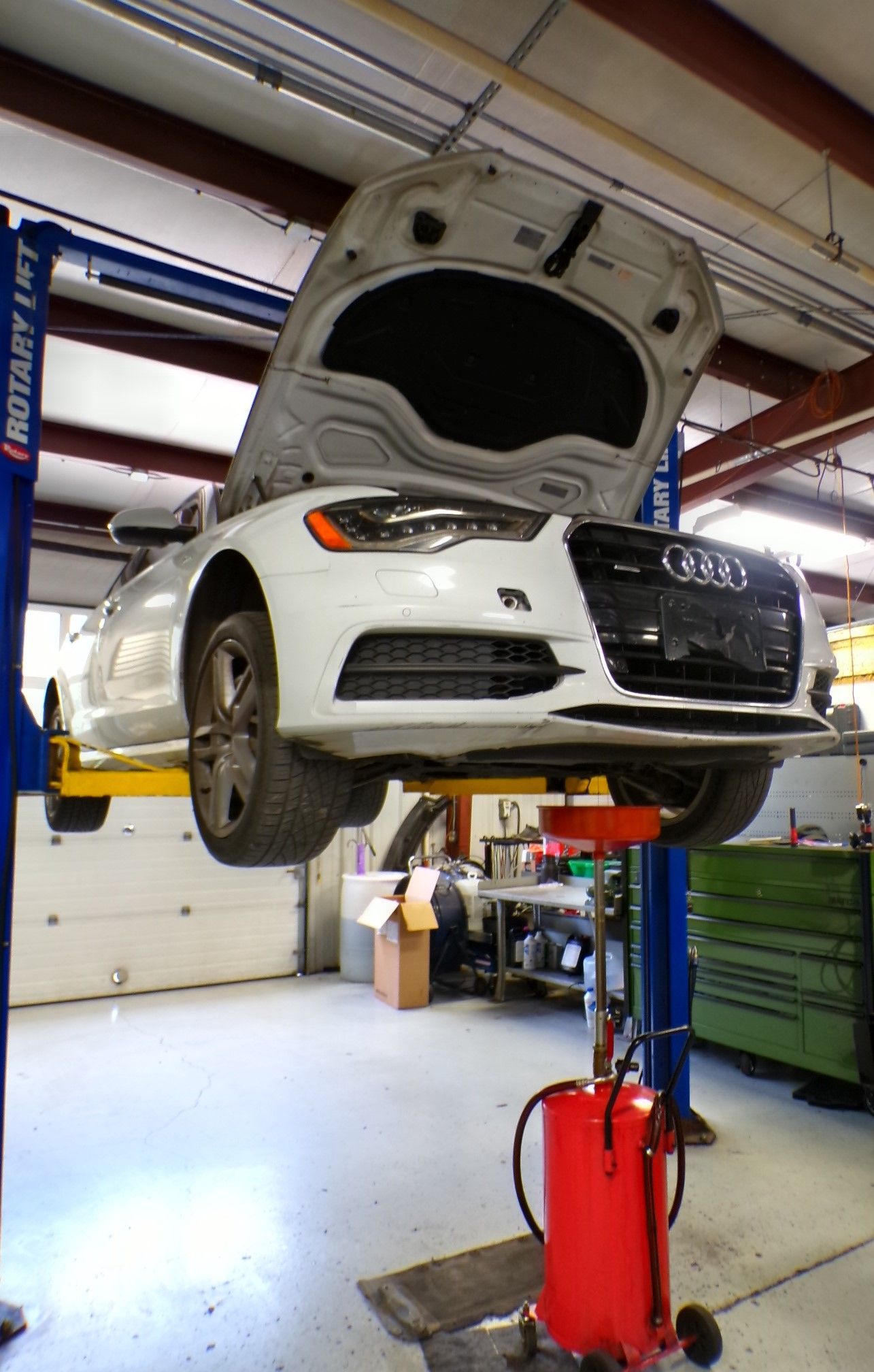 A white car with the hood up is on a lift in a garage. | Import Specialty Service