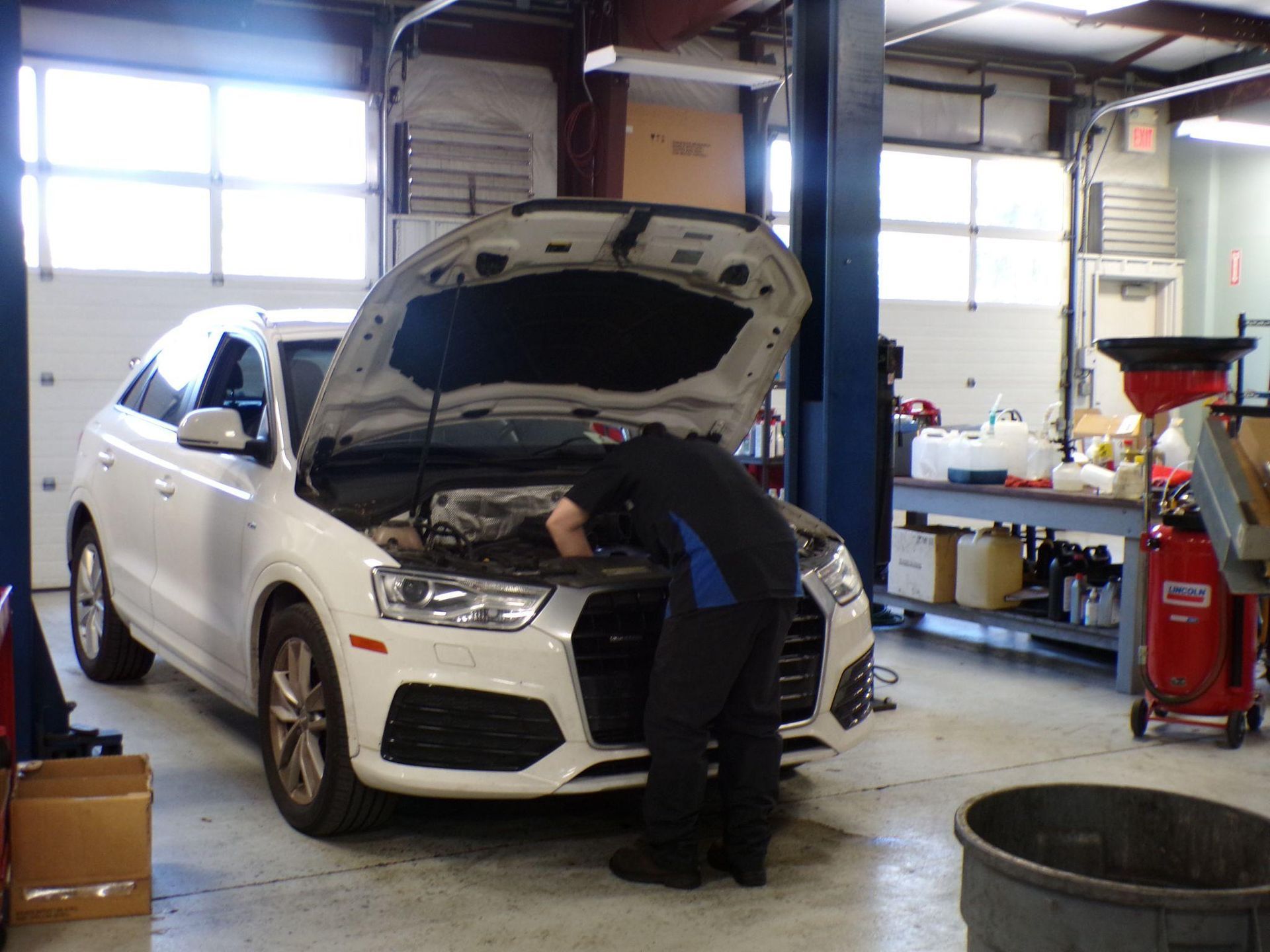 A man is working on a white car in a garage. | Import Specialty Service