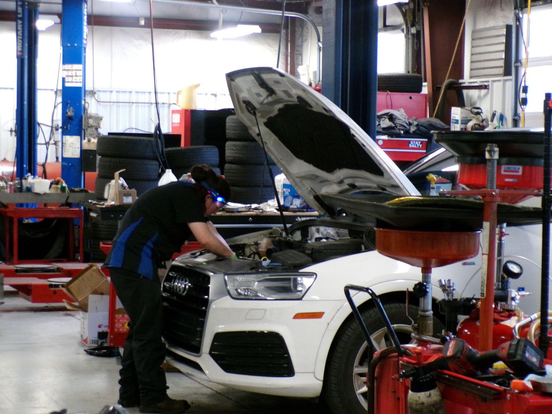 A man is working on a car in a garage with the hood up | Import Specialty Service