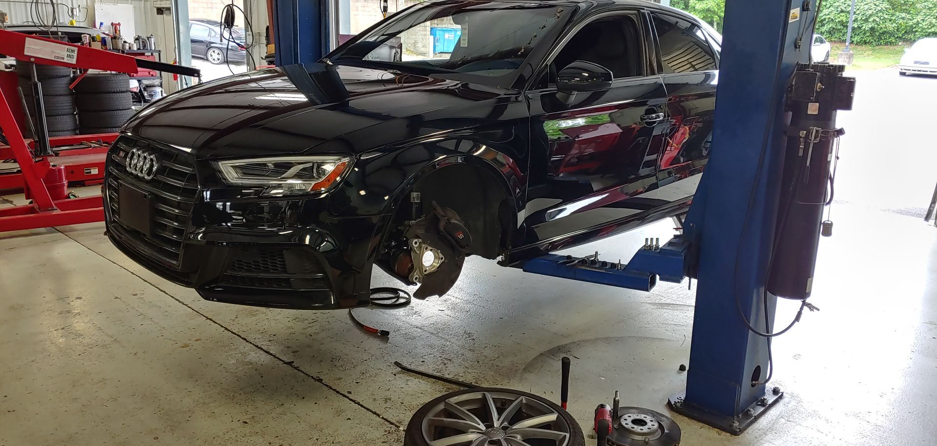 A black car is sitting on a lift in a garage. | Import Specialty Service